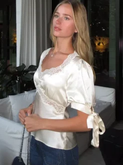 Chemisier en satin à col V bouffant et manches courtes bouffantes orné de dentelle avec ceinture à nouer dans le dos et coupe ajustée. Élégante chemise pour femme.