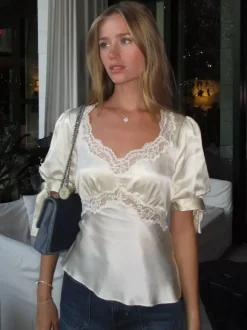 Chemisier en satin à col V bouffant et manches courtes bouffantes orné de dentelle avec ceinture à nouer dans le dos et coupe ajustée. Élégante chemise pour femme.