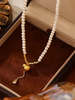 Collier élégant en perles fines orné d'un pendentif boule dorée et d'un pompon en zircon scintillant.