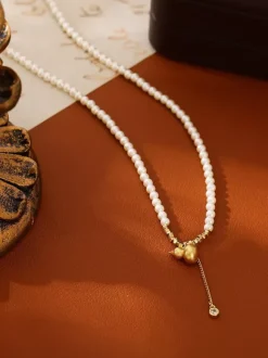 Collier élégant en perles fines orné d'un pendentif boule dorée et d'un pompon en zircon scintillant.