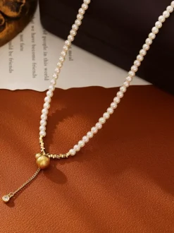 Collier élégant en perles fines orné d'un pendentif boule dorée et d'un pompon en zircon scintillant.