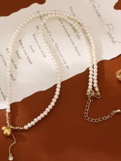 Collier élégant en perles fines orné d'un pendentif boule dorée et d'un pompon en zircon scintillant.