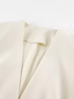 Veste blazer péplum sans manches à col en V et boutonnage nacré à une rangée de boutons.